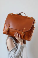 Brown leather satchel held by a person against a plain background, Obroi