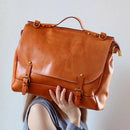 Brown leather satchel held by a person against a plain background, Obroi