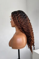 A long, dark brown to black curly wig displayed on a mannequin head and shoulders against a plain light gray background, Obroi