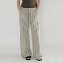 A person wearing loose, wide-leg striped pants in a light gray and beige vertical stripe pattern, paired with a dark brown top and black sandals, shown from the waist down against a plain white studio background, Obroi