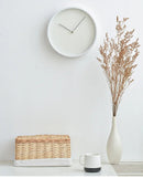 White wall clock, wicker basket, white mug, and vase with dried plants on a white surface, Obroi