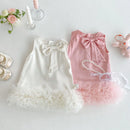 Two children's dresses, one white and one pink, on a light surface with decorative items, Obroi