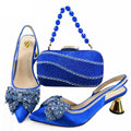 A coordinated women's formal outfit set on a white background, including two blue satin slingback heels with large embellished bows, a matching rhinestone clutch bag with a beaded handle, and a small gold ring clasp, Obroi