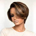 A woman wearing a short, layered wig with dark brown and warm blonde highlights, styled with a side-swept fringe, against a plain light background, Obroi