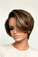 A woman wearing a short, layered wig with dark brown and warm blonde highlights, styled with a side-swept fringe, against a plain light background, Obroi