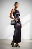 Woman in a long purple dress holding a black handbag against a white background, Obroi