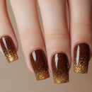 Close-up of a hand with brown and gold glittery nail polish on a neutral background, Obroi