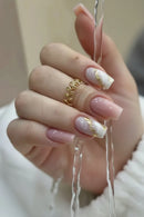 Hand with pink and gold nail design wearing a gold ring on a soft background, Obroi