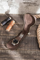 Brown leather watch case with a watch on a wooden surface with spools of thread and rope, Obroi