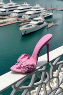 Pink high-heeled shoe with floral design on a railing by a marina, Obroi