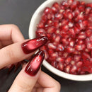 Hand with red nail polish holding a pomegranate seed next to a bowl of pomegranate seeds, Obroi