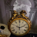 Decorative clock with gold casing and cherub figures against a patterned wall, Obroi