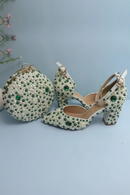 Decorative shoes and matching round clutch with green gemstones on a light blue background, Obroi