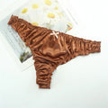 Brown satin thong on a white surface with a magazine in the background, Obroi
