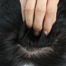 Close-up of a hand lifting a section of black hair to show the hairline and texture of a hairpiece or wig, Obroi