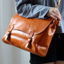 Brown leather bag with gold accents held by a person wearing a blue shirt, Obroi