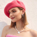 Woman wearing a pink beret and pearl necklace against a light background, Obroi