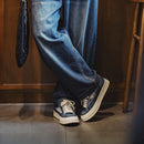 Person wearing blue jeans and matching sneakers in a room with wooden floor and wall, Obroi