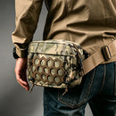 A tactical crossbody bag with a camouflage pattern and a prominent honeycomb-style brown front panel, worn by a person in a khaki jacket and blue jeans, Obroi