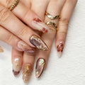 Close-up of hands with decorative nail art featuring gold and brown designs on a white background, Obroi