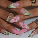 Close-up of a hand with pink floral nail art on a neutral background, Obroi