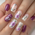Nails with floral and leaf designs in purple, pink, and white on a neutral background, Obroi