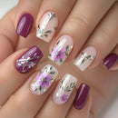 Nails with floral and leaf designs in purple, pink, and white on a neutral background, Obroi
