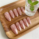 Set of pink nail extensions on a wooden tray with a glass of water and mint leaves, Obroi