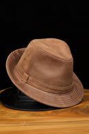 Brown leather hat on a wooden surface with a black background, Obroi