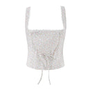 A sleeveless white crop top with a tiny multicolor floral print, scalloped lace trim at the neckline and straps, and a drawstring tie at the center front, shown against a plain white background, Obroi