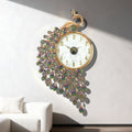 A decorative wall clock shaped like a peacock, with a gold-tone frame, white oval face, iridescent teardrop crystals, and a peacock head at the top, mounted on a light gray wall above a white sofa. Chinese text appears along the bottom edge, Obroi