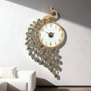 A decorative wall clock shaped like a peacock, with a gold-tone frame, white oval face, iridescent teardrop crystals, and a peacock head at the top, mounted on a light gray wall above a white sofa. Chinese text appears along the bottom edge, Obroi