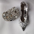 Silver jeweled shoe and heart-shaped brooch on a light gray background, Obroi