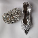 Silver jeweled shoe and heart-shaped brooch on a light gray background, Obroi