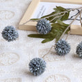 Decorative gray flowers on a branch with green leaves on a textured white surface, Obroi