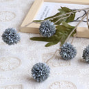 Decorative gray flowers on a branch with green leaves on a textured white surface, Obroi