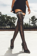 Person wearing black studded high-heeled shoes and stockings outdoors, Obroi