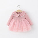 A pink long-sleeve baby dress with a ribbed knit bodice, white scalloped Peter Pan collar, and a layered tulle skirt, hanging on a wooden hanger against a plain white background, Obroi