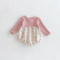 A baby long-sleeve romper laid flat on a light textured background. The top is a dusty pink ribbed knit, and the ruffled bloomers are cream with a pink floral and bunny print, Obroi