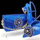 Blue sequin clutch and high-heeled shoes with floral embellishments on a black background, Obroi
