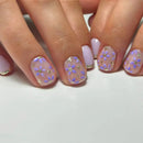 Close-up of hands with pink and purple floral nail design on a white background, Obroi