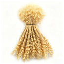 A bundle of curly dreadlock hair extensions in a light blonde color, tied with a black elastic band, shown against a plain white background, Obroi