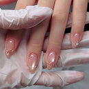 A close-up of manicured fingernails with a glossy nude-pink base, small pink bow details, and tiny gold accents, shown with a white gloved hand holding the fingers, Obroi