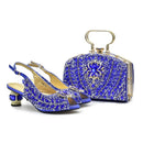 A matching royal blue beaded evening shoe and handbag set on a white background. The set includes a pair of open-toe slingback heels with chunky beaded blue and gold block heels, and a structured rectangular handbag with a top handle, both covered in blue and gold beadwork, Obroi