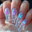 A close-up of a hand showcasing coffin-shaped press-on nails with a clear acrylic base decorated with colorful butterfly and star designs, Obroi