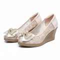 Pair of beige wedge shoes with floral lace and bow details on a white background, Obroi