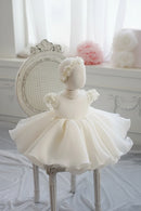 White children's dress with floral details on a mannequin against a decorative background, Obroi
