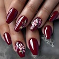 Close-up of hands with burgundy nail polish and floral designs on a gray background, Obroi