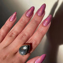 Hand with pink glittery nails and a decorative ring on a neutral background, Obroi