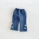 A pair of toddler blue denim pants with an elastic waistband, featuring three small heart-shaped embellishments on each leg, laid flat on a light textured background, Obroi